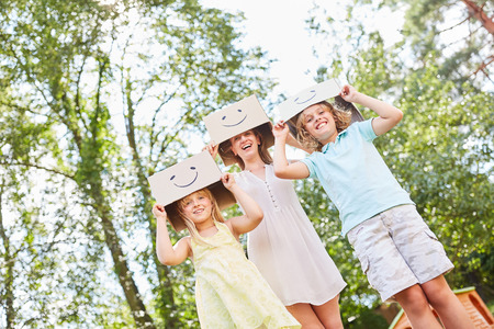 Mother and kids play with funny painted cardboard boxes in the gardenの写真素材