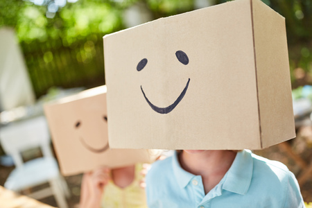 Child plays under a cardboard box funny painted with a faceの写真素材