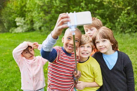 Laughing group of kids together is taking a selfie with smartphone on selfie stickの写真素材