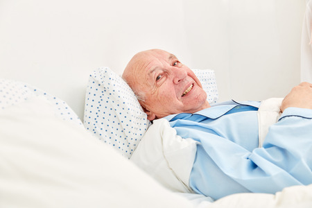 Senior is sick and frail in bed as a patient in a nursing home or hospiceの写真素材