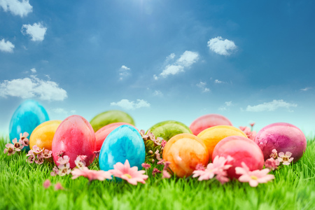 Many colorful easter eggs lie at Easter on a green meadow in front of a blue sky