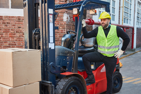 Man as a forklift driver stands in front of his forklift with packages as cargoの写真素材