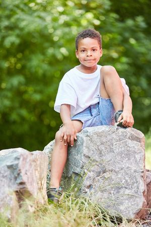 African boy sits relaxed on a stone in the park in summerの写真素材