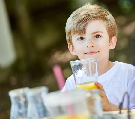 Boy drinks a glass of healthy orange juice at the summer camp for breakfastの写真素材