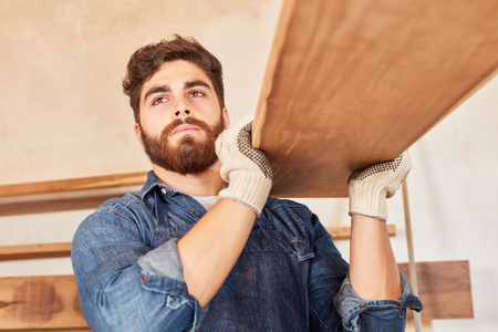 Young man as carpenter or carpenter in training carries wooden beamsの写真素材