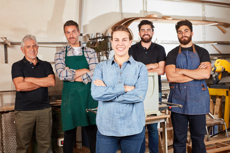 Smiling woman as apprentice in carpentry in front of carpenter colleagues in workshopの写真素材