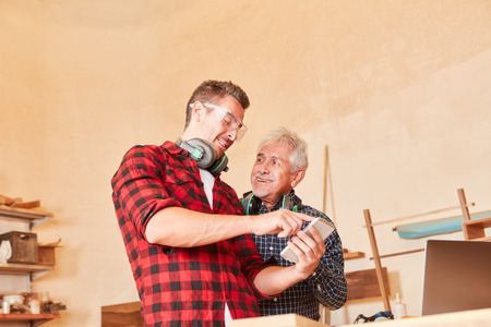 Young craftsman with smartphone writes a text message in the joinery workshopの写真素材