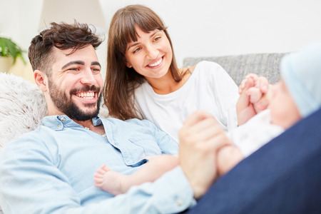 Happy parents are lying on the sofa and playing with their little babyの写真素材