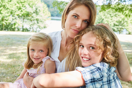 Happy mother lovingly hugs her two children on a meadow in the summer in the park