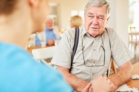 Nursing woman consoles senior man while holding his hands in retirement homeの写真素材