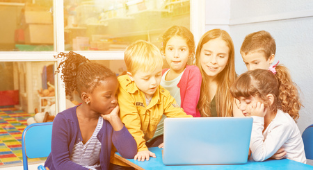 Kids play together at laptop computer with educator in kindergarten