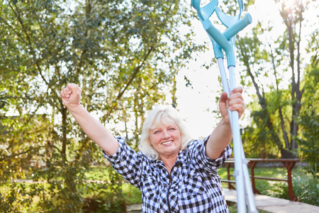Cheering senior woman with crutches in rehab clinic after running workoutの写真素材