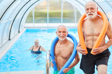 Two men in a swimming pool with swimming noodle are looking forward to aqua fitnessの写真素材