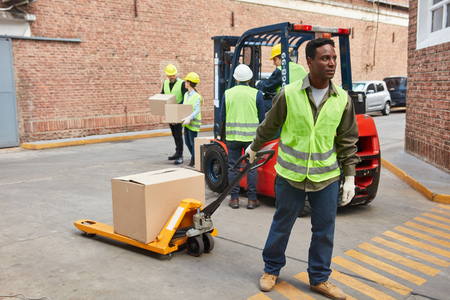 African worker in front of the logistics center with package on the pallet truck