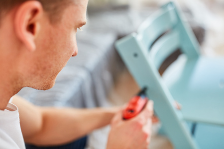 Man as a home improvement uses a drill screwdriver to assemble a chairの写真素材