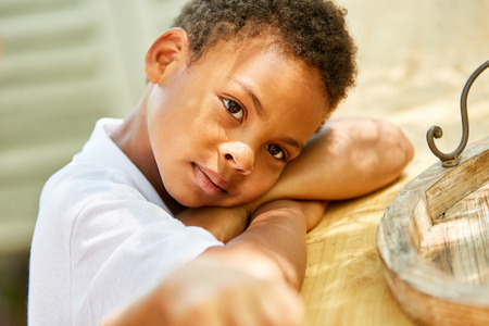 African boy tiredly lays his head on his arms and dreams to himselfの写真素材