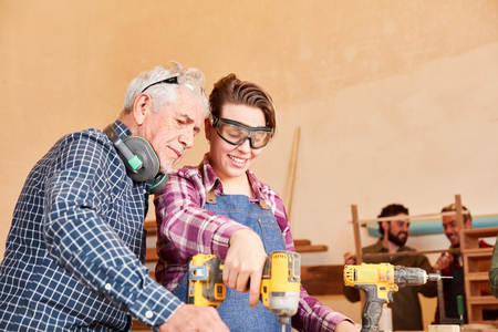 Senior craftsman master supervises young woman training as a carpenterの写真素材
