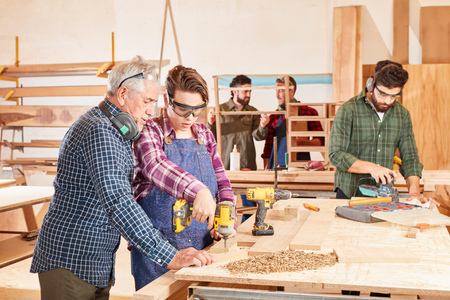 Master and wife apprentice with drill at woodworking workshopの写真素材