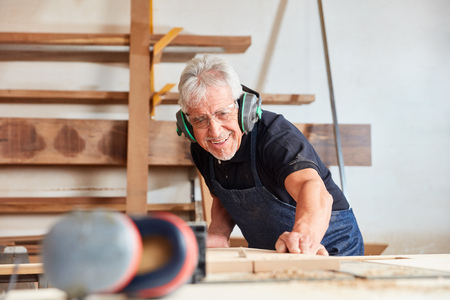 Old carpenter saws wood at the circular saw in carpentry or cabinetmakingの写真素材