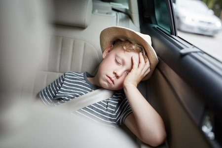 Boy with hat is sleeping on the back seat in the car on the road trip on vacationの写真素材