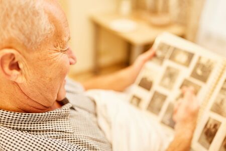 Old man with dementia or Alzheimer's in nursing home looks at a photo albumの写真素材