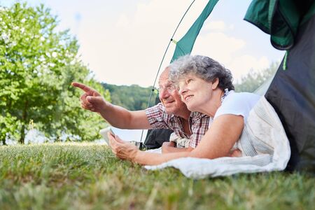 Senior couple camping in nature in tent with a tablet computerの写真素材