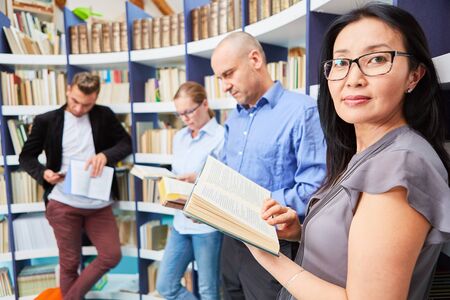Asian woman reading book together with young people in university library