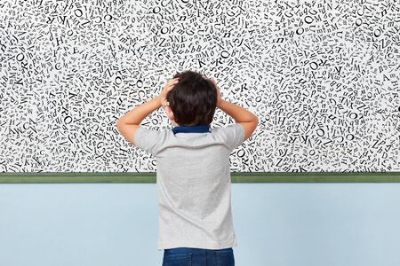 Child with dyslexia is standing in front of a whiteboard with many letters in elementary schoolの写真素材