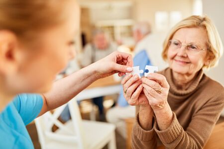 Nursing lady helps a demented elderly woman play puzzle in retirement homeの写真素材