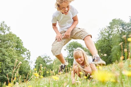 Boy in leapfrog with his sister on a meadow in summer