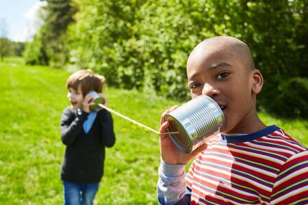 African boy speaks into a can phone with cord in the sunshine in the parkの写真素材