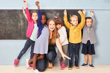 Cheering children and teacher together at the blackboard of a preschool or elementary schoolの写真素材