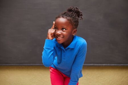 African girl as a clever pupil in front of a blackboard in elementary school has an ideaの写真素材