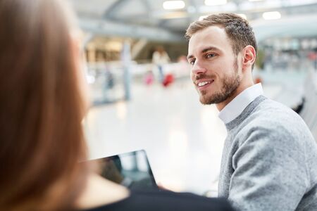 Young man with laptop computer talking to a woman in the airport terminal