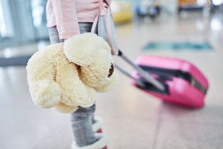 Alone traveling child with cuddly toy and trolley suitcase in the airport terminal during the holidaysの写真素材