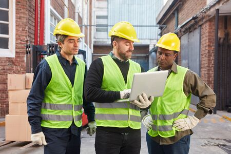 Â Three logistics workers with laptop computer in front of warehouse of freight forwarderの写真素材
