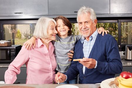 Happy grandson between granny and granddad in the morning in the kitchen having breakfast