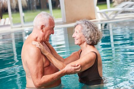 Smiling senior man helping his wife to swim while learning in the poolの写真素材