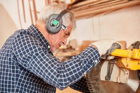 Old carpenter saws wood at the chop saw in carpentry or joineryの写真素材