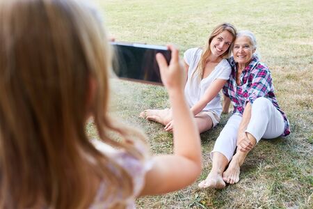 Little girl photographs granny and her mother in the garden with the smartphone