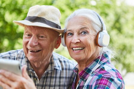 Couple of seniors with headphones and tablet computer listens to music in nature in summerの写真素材