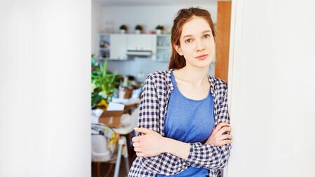 Young woman is leaning against door in new apartment after movingの写真素材