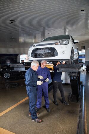 Mechanic team in the workshop at the main inspection with car on the liftの写真素材