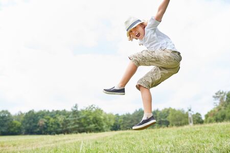 Happy boy plays and jumps hilariously on a summer meadow