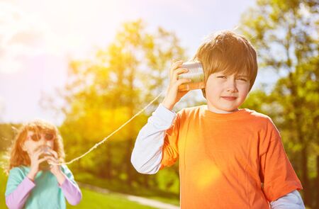Children speak in a tin can telephone with cord in the summer