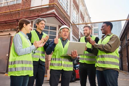 Successful logistics team with laptop computer stands in front of a factory hall