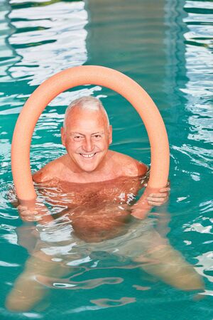 Senior man with swimming noodle doing aqua fitness in a swimming pool