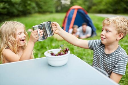 Two kids eat cherries and drink out of cups while camping in natureの写真素材