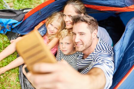 Happy family on vacation is taking a self portrait with the smartphone in the tentの写真素材