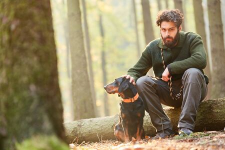 Forester is sitting on a log with a hound as a hunting dog in the woodsの写真素材